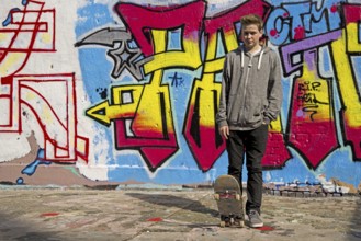 Thirteen-year-old boy with skateboard in front of graffiti, Cologne, Germany, Europe