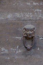 Old door knocker in the shape of a face on a weathered stone surface, Galatina, Apulia, Italy,