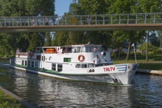 White boat under a bridge on a canal with trees in the background, boat Talty on a canal between