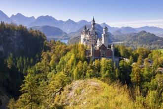 Neuschwanstein Castle rises against a picturesque backdrop of mountains and autumnal forest,