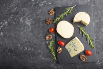 Blue cheese and various types of cheese with rosemary and tomatoes on black slate board on a black