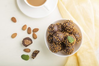 Chocolate caramel ball candies with almonds and a cup of coffee on a white wooden background and