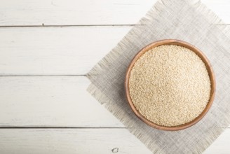 Wooden bowl with raw white quinoa seeds on a white wooden background and linen textile. Top view,