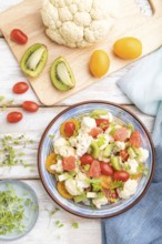 Vegetarian salad of cauliflower cabbage, kiwi, tomatoes, microgreen sprouts on white wooden