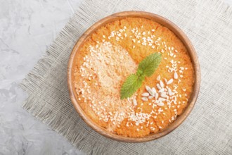 Carrot cream soup with sesame seeds in wooden bowl on a gray concrete background with linen textile