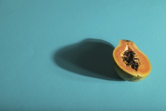 Ripe cut papaya on blue pastel background. Side view, copy space, hard light. Tropical, healthy