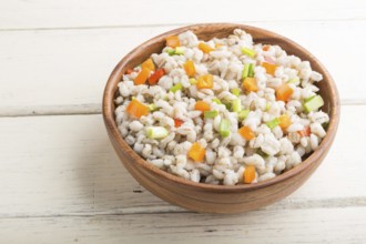 Pearl barley porridge with vegetables in wooden bowl on a white wooden background. Side view, close