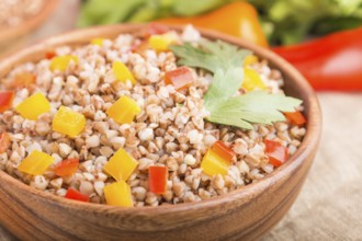 Buckwheat porridge with vegetables in wooden bowl on a white wooden background and linen textile.