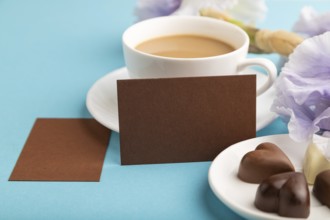 Brown business card with cup of cioffee, chocolate candies and iris flowers on blue pastel