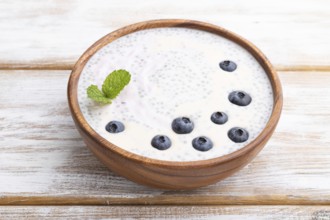 Yogurt with blueberry in wooden bowl on white wooden background. Side view, close up