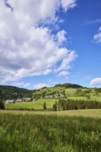 Landscape with hills, meadows, forests and a village under a blue sky with cumulus clouds near