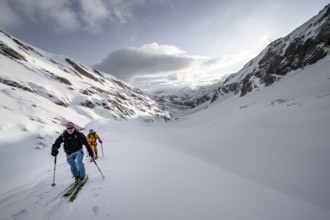 Two ski tourers in a snowy mountain landscape in the morning light, view into the Iffigtal, cloudy