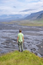 Hiker, young man on a hill, view over alluvial land, meandering river, Dímonarhellir, Suðurland,