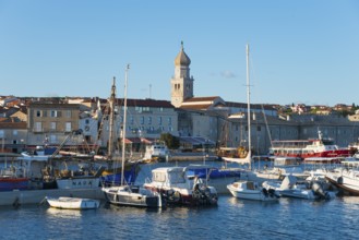 Coastal town at sunset with harbour and boats, in the background a church and historical buildings,