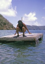 Woman wearing swimwear with snorkel and mask crouching on diving platform oil the sea, island of