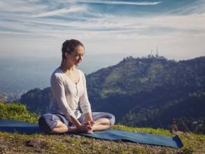 Sporty fit woman practices yoga asana Baddha Konasana, bound angle pose outdoors in HImalayas