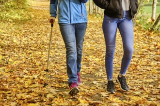 Two young teenage girls walk through colourful autumn leaves, one with a crutch, the other without