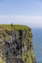 Tourist at the edge of a rock cliff, steep coast, at Reynisfjara beach, Vik, South Iceland,