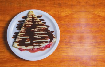 Crepe with chocolate cream and strawberry on wooden table. Sweet strawberry crepe with chocolate