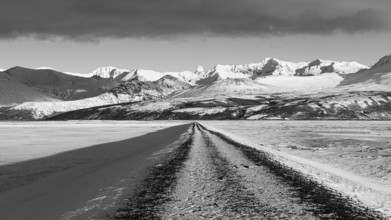 Unpaved road towards the snow-covered mountains of Skaftefellsjöll, black and white photo, near