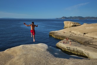 Sarakiniko, Greece, May 23, 2019: Young tourists jump off the white rocks cliff on famous tourist