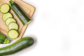 Courgettes (Cucurbita pepo), whole and cut open, on wooden board, on white, copy room