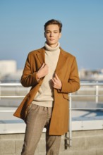 Spring, autumn outfit. Street fashion. Young man in checkered trousers, sweater wraps wool coat