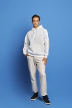 Attractive stylish man wearing white sweatshirt and sweatpants standing over blue studio background