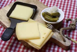 Raclette, cheese slices on wooden board and in raclette pans, Switzerland, Europe