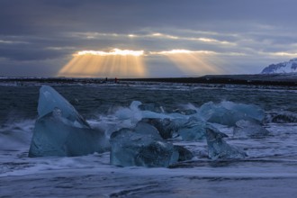 Waves breaking on icebergs on the black beach of Breidamerkursandur, sunset, near Jökullsarlon,