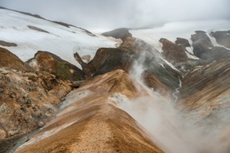 Steaming streams between colourful rhyolite mountains and snowfields, Hveradalir geothermal area,