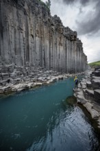 Tourist standing by the river in Stuðlagil Canyon, turquoise blue river between basalt columns,