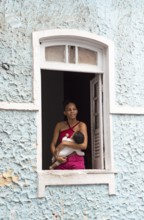 Brazilian woman with baby in her arms standing at a window, historic old town, Salvador, state of