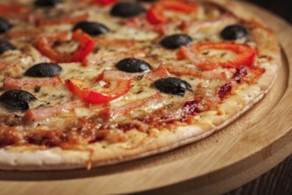 Ham pizza with (capsicum) and olives on wooden board on table close up