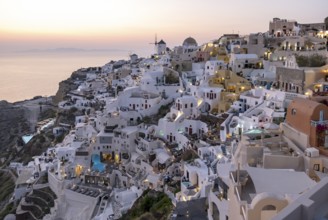 Cliff-side houses, villas and windmill in the village of Ia seen from Oia Castle at dusk,