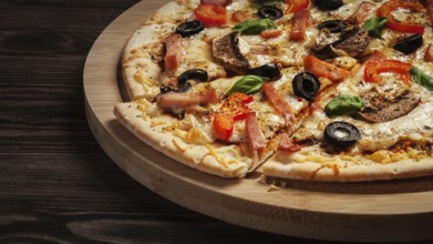 Letterbox panorama of sliced ham pizza with (capsicum) and olives on wooden board on table