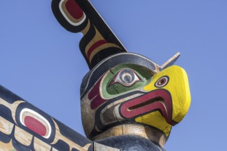 Colourful wooden carved Canadian totem pole showing eagle's head against blue sky