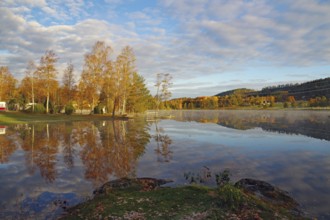 Jetty, trees and houses reflected in the water of Bullaren, lake, October, Bohuslän, Sweden on a