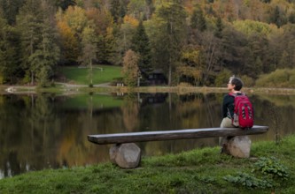 Older woman with backpack, Best Ager, sitting lonely on wooden bench, Ebnisee, Kaisersbach, autumn,