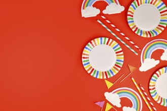 Rainbow themed party flat lay with colorful plates, napkins and drinking straws on red background