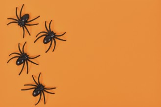 Plastic spiders on side of bright orange Halloween background with empty copy space