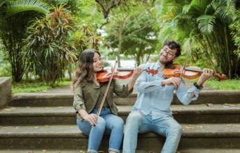 Portrait of two young violists playing violin sitting on stairs outside. Portrait of smiling