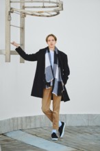 Full length portrait of young man in old wool coat, scarf and short trousers leaning to fire escape