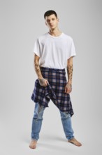 Young cocky man in t-shirt, jeans and checkered shirt tied at the waist