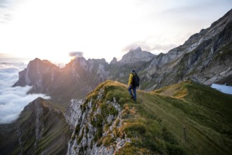 Hiker enjoying the view over the Säntis mountains into the valley of Meglisalp at sunrise, high fog