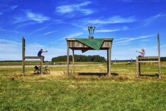 Oversized table with two chairs on a meadow, passers-by taking a break together, having fun, sunny