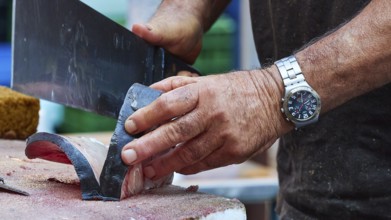 Man cuts tuna into strips with large knife, fish market, old town, Catania, east coast, Sicily,