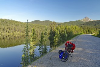 Bicycle standing by a crystal clear lake on an empty road, evening light, Stewart Cassiar Highway,