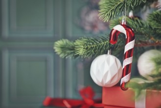 Candy cane christmas ornament on tree with gifts on side of green background