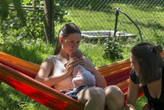 Young mother with baby in a hammock in the garden, sister on the right, Mecklenburg-Vorpommern,